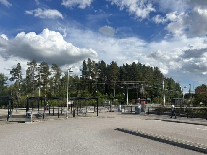 Empty train station with bike racks, under a partly cloudy sky, near a wooded area, showcasing modern urban transportation infrastructure in a serene setting.