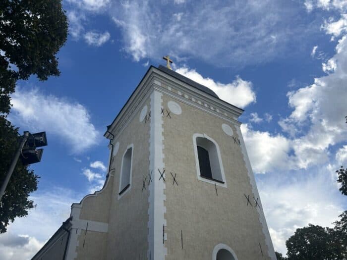 Historic church tower with cross on top under a blue sky with clouds, highlighting architecture and religious heritage.